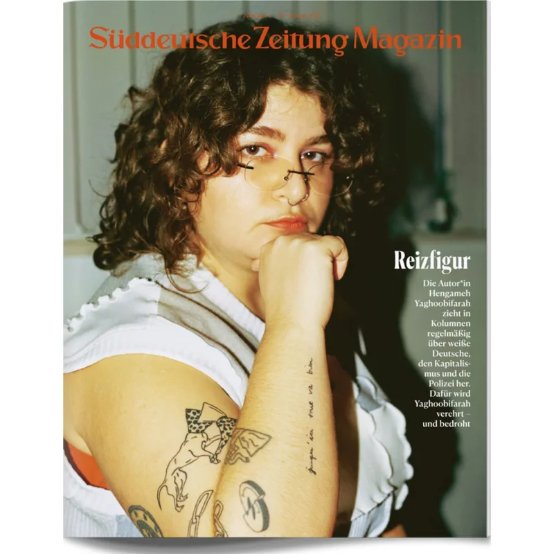 Eine Person mit lockigem Haar und Tattoos posiert nachdenklich auf dem Cover des Süddeutsche Zeitung Magazins.