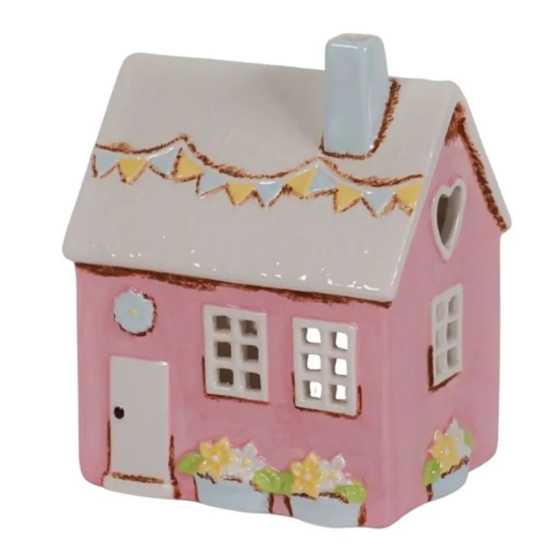 Das "Isabelle Rose - Keramik Haus als Teelichthalter im Landhausstil Rosa" ist ein kleines, rosafarbenes Keramikhaus mit grauem Dach, blauem Schornstein, Wimpeln, Blumenkästen und einem herzförmigen Fenster.