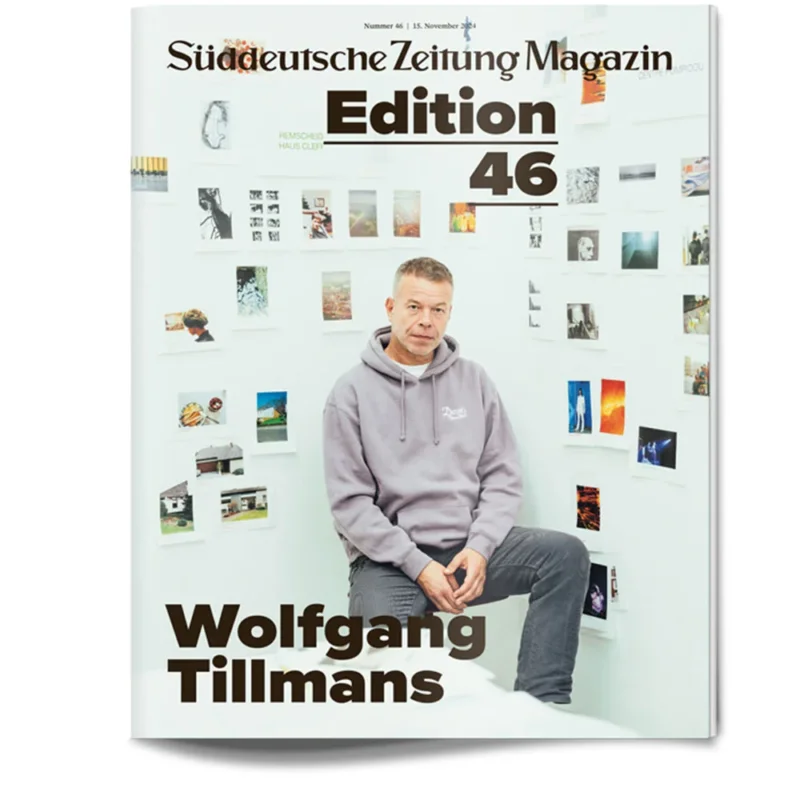 Ein Mann in einem Kapuzenpulli sitzt vor einer Wand, die mit Fotos auf dem Cover des Süddeutsche Zeitung Magazins bedeckt ist.